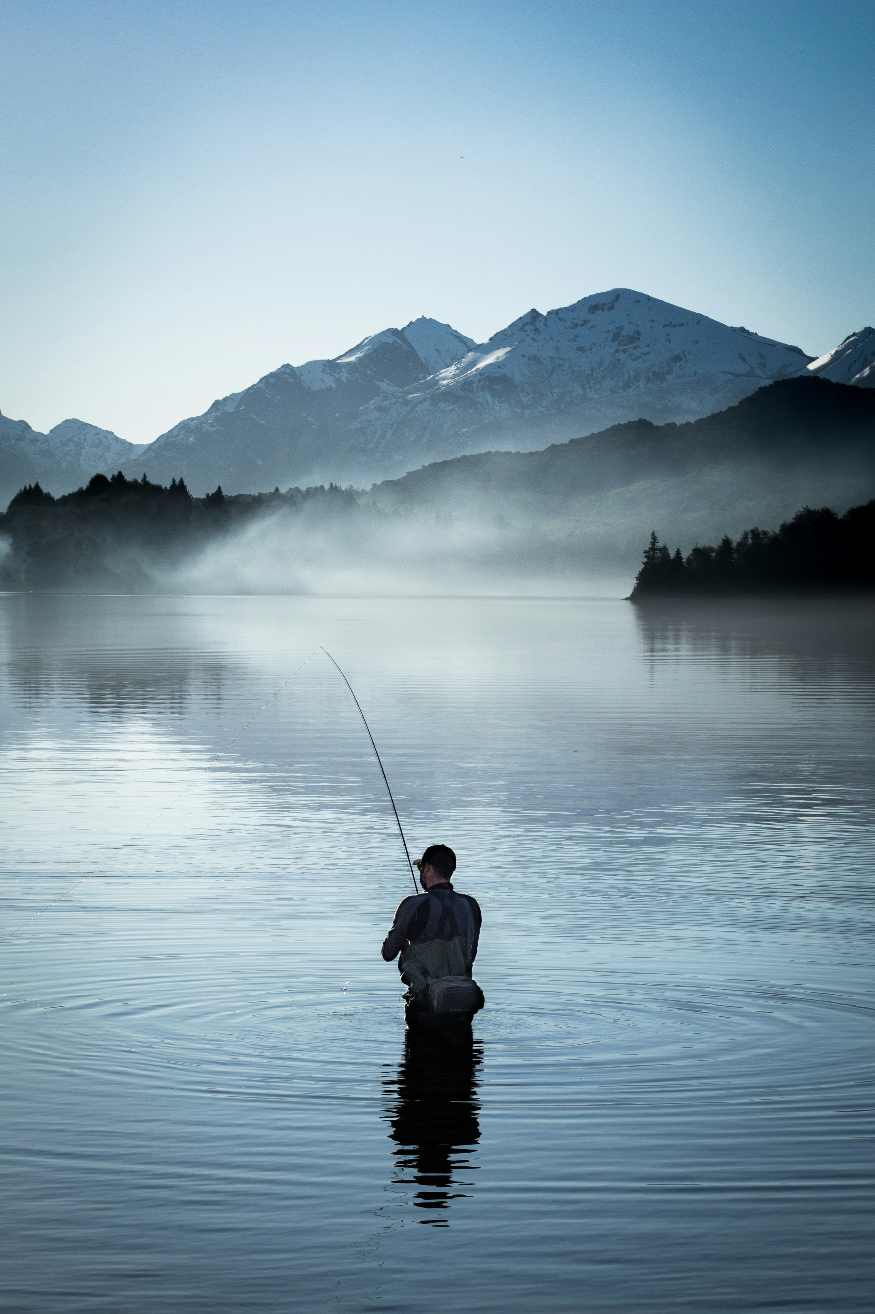 Fly fisherman wading in a misty mountain lake at dawn